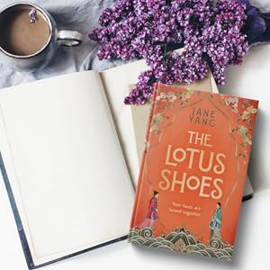 Orange book on blank open book next to coffee in a mug and purple flowers