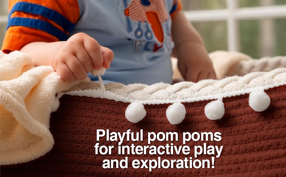 Baby in changing basket with fleece blanket playing with pom poms