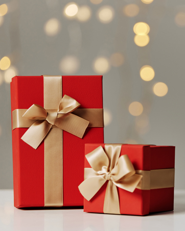 Two red gift boxes with gold ribbon bows, one larger and one smaller, displayed against a blurred background with golden bokeh lights.