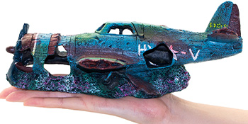 Dekoratives Aquarium-Ornament in Form eines versunkenen Vintage-Flugzeugs. Blaugrüne Farbe mit korallenähnlichen Texturen, in der Hand einer Person gehalten.