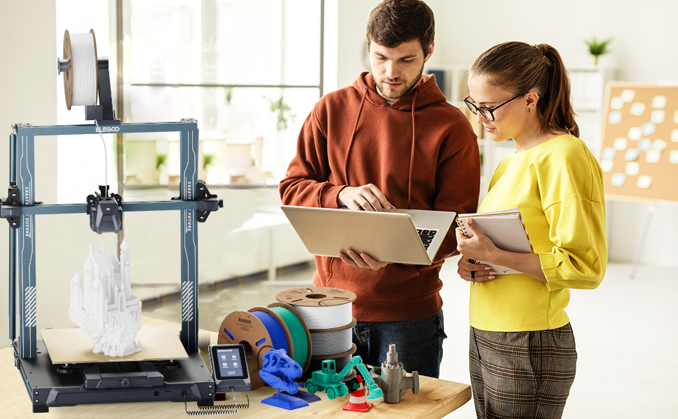 Configuração de impressora 3D com objetos impressos coloridos exibidos, enquanto duas pessoas examinam documentação ou planos em tablets.