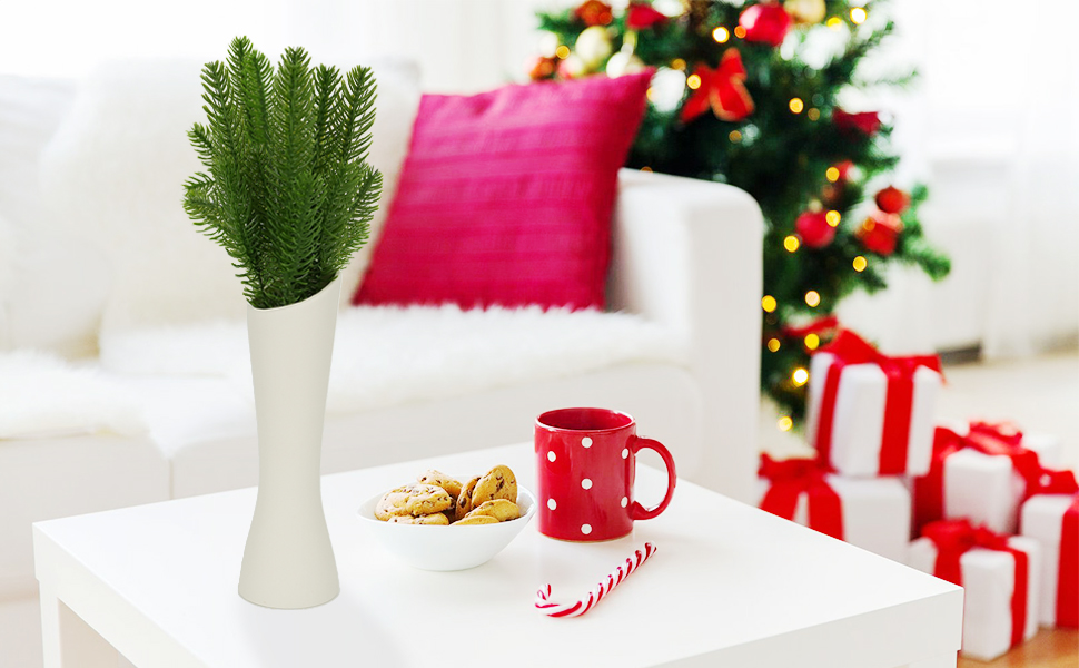 Festive holiday scene with Christmas decorations. White interior featuring wrapped presents with red bows, a red mug, and green plant in white vase against light background.