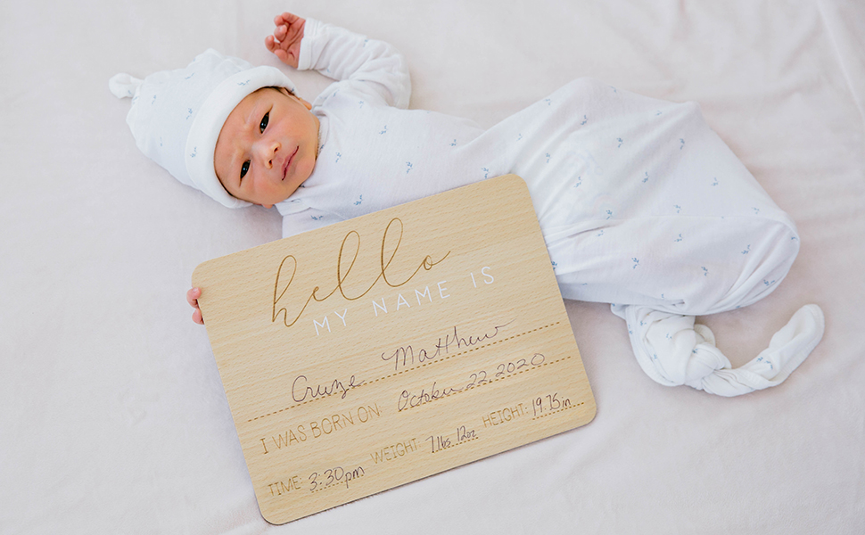 Newborn baby laying next to baby arrival photo prop sign