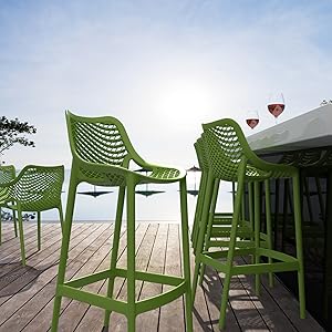 sur terrasse en bois. Les chaises ont un design moderne et perforé. L'océan ou une grande étendue d'eau visible en arrière-plan.