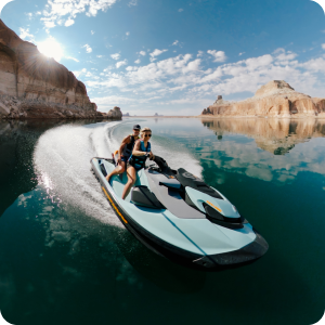 Dos motos acuáticas recorriendo aguas azules cerca de acantilados rocosos bajo un cielo soleado. Los ciclistas crean un espectacular rocío de agua mientras maniobran una embarcación a gran velocidad.