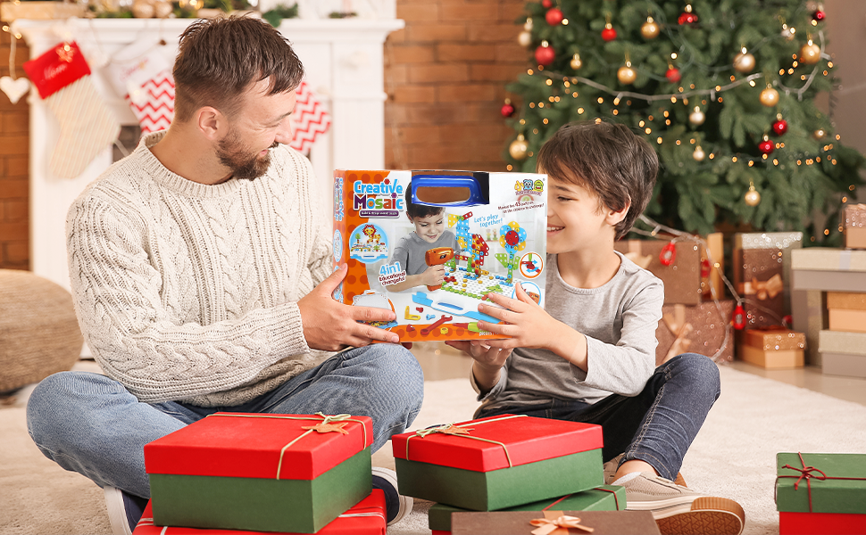 Holiday scene with decorated Christmas tree in background, showing two people sitting on floor with red and green gift boxes nearby.