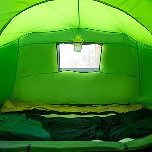 Vista interior de una tienda de campaña de color verde neón brillante con área para dormir y panel de ventana en el techo, que muestra los sacos de dormir dispuestos.