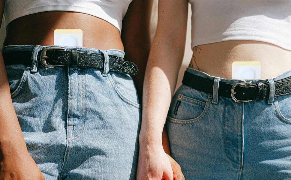 Midsection of two people wearing light-colored tops and blue jeans with black belts, standing side by side.