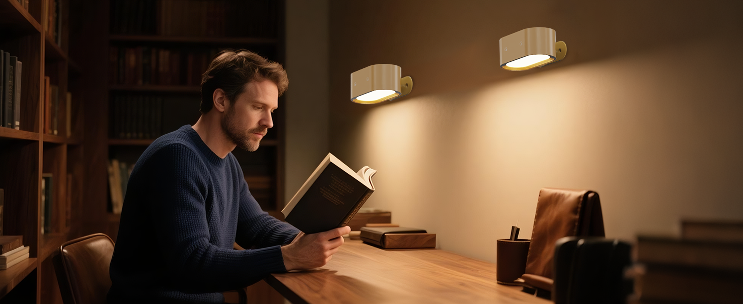 A person reading a book at a wooden desk illuminated by two wall-mounted light fixtures. Bookshelves are visible in the background, creating a cozy study atmosphere.