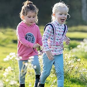 Kinder spielen draußen auf einer Frühlingswiese mit weißen Blumen. Szene aufgenommen bei natürlichem Tageslicht mit grünem Grashintergrund.