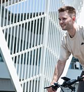 Primer plano de una persona agarrada al manillar de una bicicleta, con una camisa de color claro. Solo la parte superior del cuerpo es visible sobre un fondo