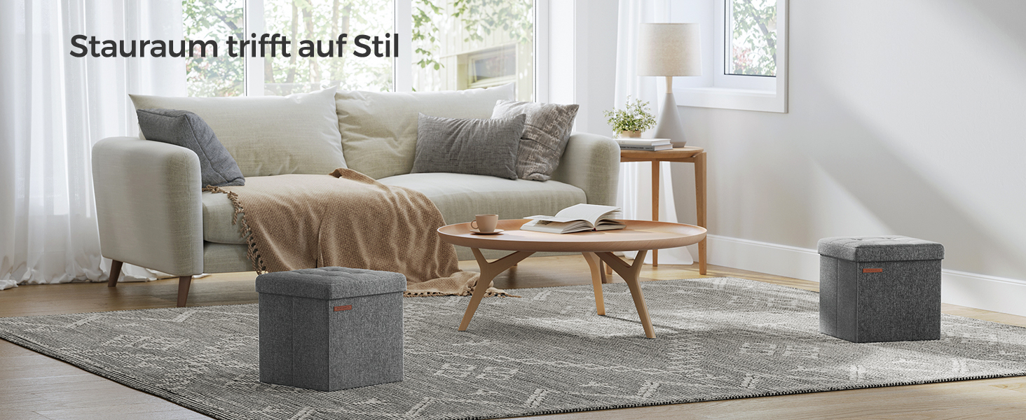 Modernes Wohnzimmer mit hellgrauem Sofa, Couchtischen aus Holz und zwei dunkelgrauen Würfelhockern auf einem gemusterten Teppich