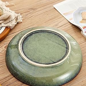 Ceramic plate with a green glazed interior and beige rim. The plate has a shallow, bowl-like shape and sits on a wooden surface.