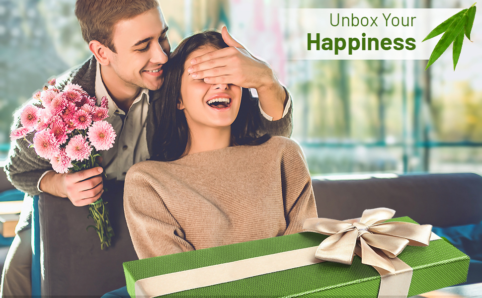 Green gift box with white ribbon on table. Text 'Unbox Your Happiness' visible in upper right corner.