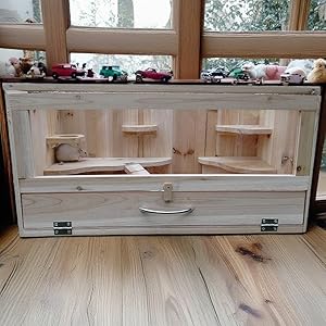 Hamsterkäfig aus Holz mit mehreren Ebenen, Rampen und Fächern. In der Nähe eines Fensters positioniert, geeignet für die Unterbringung und zum Spielen kleiner Haustiere.