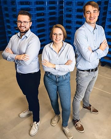 Drei Berufstätige in Business-Freizeitkleidung stehen vor einem blauen strukturierten Hintergrund.