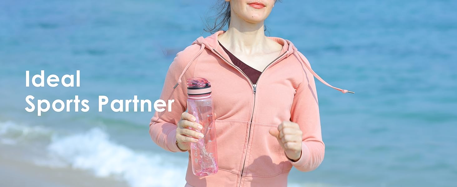 Person in pink zip-up hoodie jogging on beach, holding clear water bottle. Blue ocean in background. Text overlay reads 'Ideal Sports Partner'.