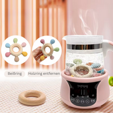 Electric food steamer with glass container, steaming. Multiple attachments shown, including teething rings and bottle holders. Digital control panel visible.