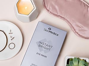 eye mask on cream colored table with a candle, silk eye mask, plant next to it.
