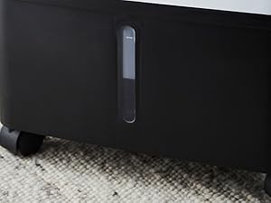 Close-up view of black electronic device or speaker with vertical light strip indicator and legs or stand visible at bottom.