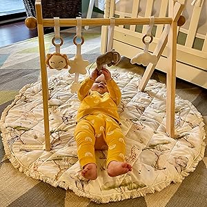 Baby lying on play mat under wooden gym playing with hanging elephant toy