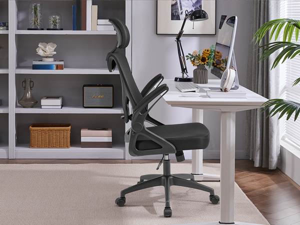 Home office setup with white desk, black ergonomic office chair, gray bookshelf, and decorative items. Natural light from window visible.