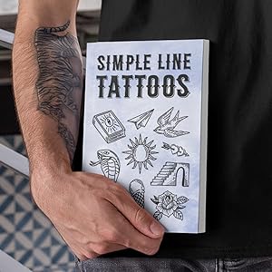 A man with a tattoo holding a tattoo book with the title 'Simple line tattoos'