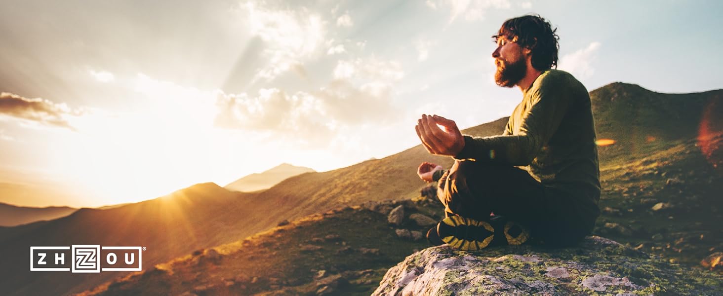 Man meditating on rock in mountains as the sun is rising.