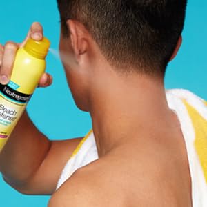 Man applying Neutrogena Beach Defense Spray Sunscreen with broad spectrum SPF to shoulder