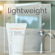 Top ¾ of face wash bottle in foreground with bathroom sink, mirror, and backsplash in background